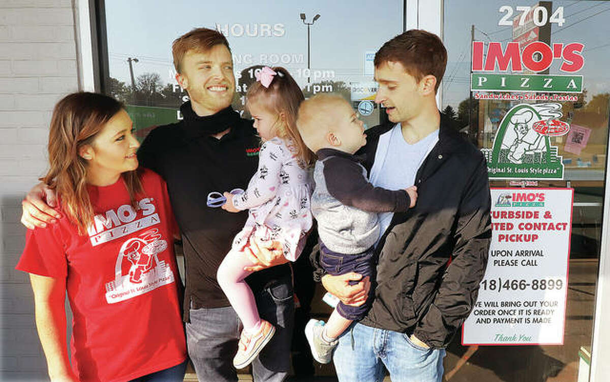 Hayden and Tyler Shereck, left, with their children, Ava, 2, and Luke, 1 — along with Imo’s Pizza co-owner Thomas Shereck, right — are upbeat and plan to rebuild following the fire that extensively damaged the interior of the restaurant early Friday morning at 2704 Godfrey Road.