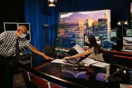 Journalism Professor Ben Davis reaches for a script from anchor Amanda Alvarado in the television studio as they prepare to record an episode of the Valley View News show in their television news class on campus at CSU Northridge in Northridge, California September 28, 2020. Due to the pandemic, students must wear masks (except the anchors when the show is recording), keep distances when possible, and wipe down their stations for safety.