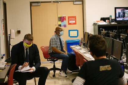 Student Anchor Ryan Ketcham (left) goes over notes as Professor Ben Davis (center) speaks to students, including student Video Coordinating Producer Bryce Wayne (right), inside the newsroom before recording an episode of the Valley View News show in their television news class on campus at CSU Northridge in Northridge, California September 28, 2020. Due to the pandemic, students must wear masks (except the anchors when the show is recording), keep distances when possible, and wipe down their stations for safety.
