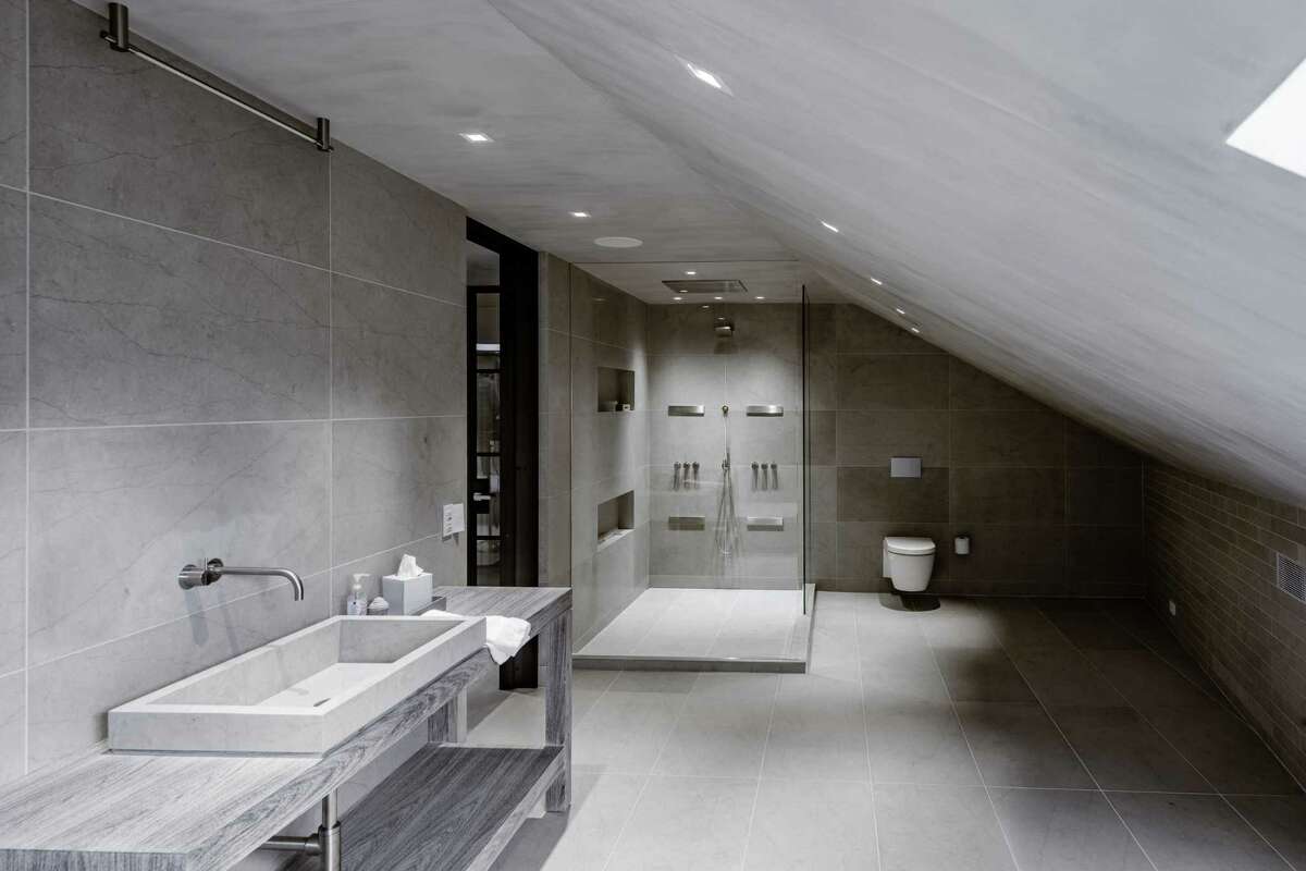 A sizable spa-like bath features a trough sink and large glass shower. Features that elevate form and function are incorporated into the design, including geothermal heat, Tischler windows, an artisanal leather tile floor in the third floor gym, Belgian plaster walls, a heated driveway, wide-plank European wood floors, limestone baths and a stairwell to the third floor with a custom lighting fixture. The bathrooms were gutted and upgraded during the construction project and the gourmet kitchen was renovated raising it to a higher level than when the house was originally built.