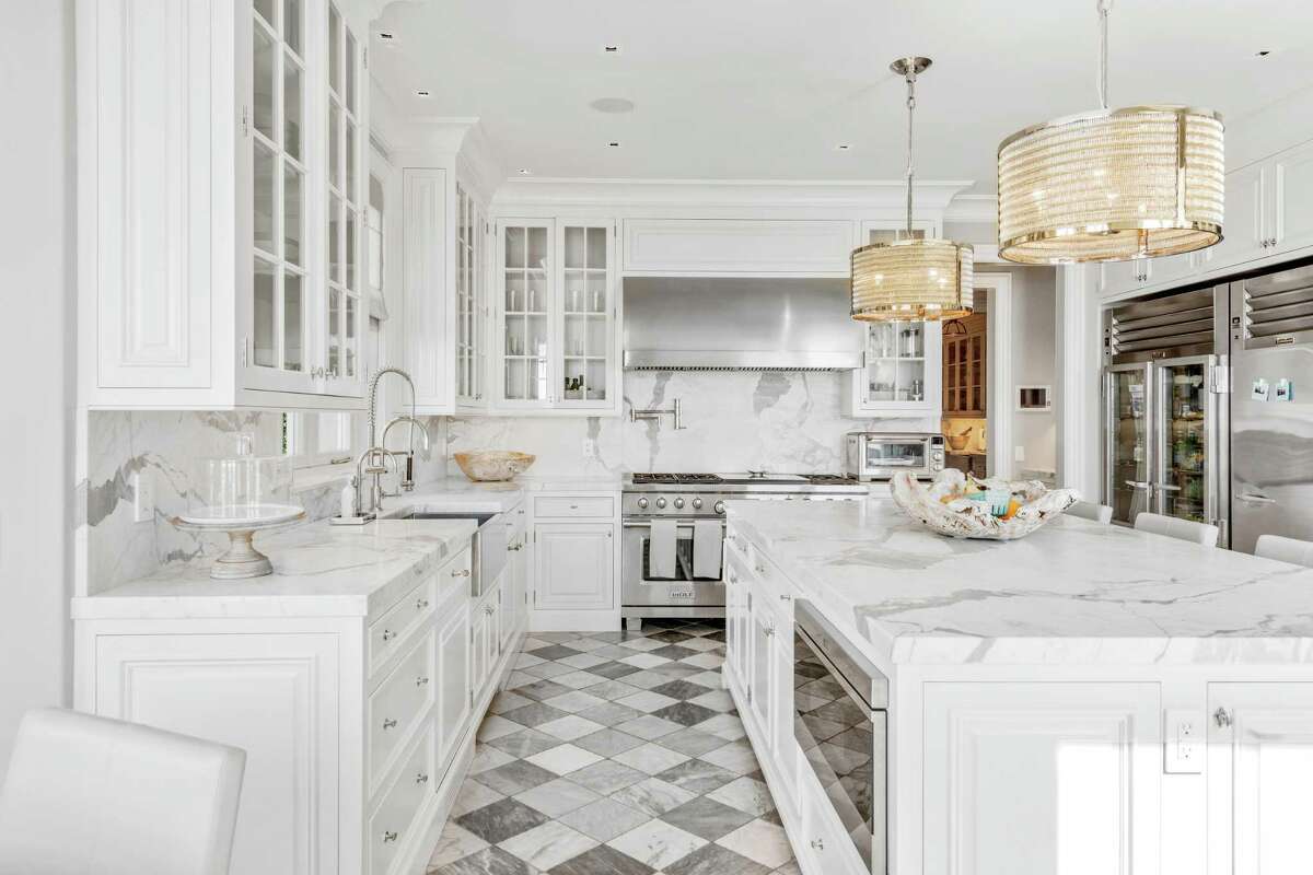 In the gourmet kitchen features include a center island, marble counters and backsplash, and commercial grade stainless appliances. The formal living room features a tall beamed ceiling, a fireplace, and three sets of French doors topped with arched transoms to the professionally landscaped grounds. In the formal dining room there are paneled walls with hidden china cabinet storage and a fireplace. Enhancing the entertainment value of this house is a service bar with a two-tiered marble counter and a brass sink. In front of it are French doors to the 0.68 acre, level property.