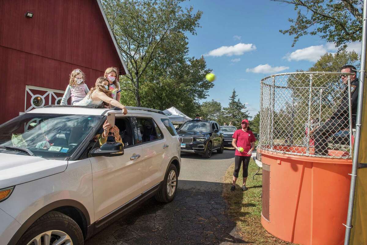 Samara White throws a ball toward the dunk tank as Sonja and Ella Kirschner look on at Ambler Farm Day on Sunday, Oct. 4, 2020, in Wilton, Connecticut. The event, which typically draws thousands of people to the farm on Hurlbutt Street, was held as a drive-in, "Cruise-thru Ambler Farm Day." Timed tickets were sold ahead of time and cars entered through the soccer field and made their way through the grounds. Farm staff and volunteers handed out everything from pumpkins for decorating, apple pies, and farm-themed treats from the Painted Cookie to a bag of old clothes and hay for families to make a scarecrow, just in time for Halloween. Cars wound their way through a hay maze and made stops for the drive-up apple slingshot, dunk tank, and shaving-cream pie throwing. Through it all, visitors were entertained by live music at the red barn.
