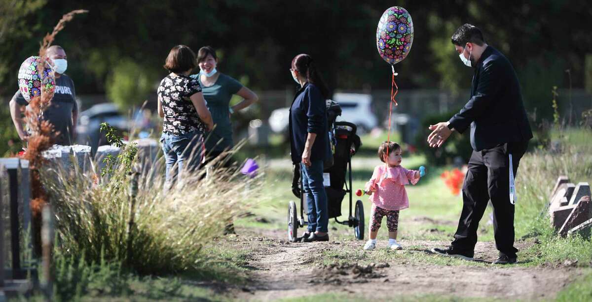Galo Gutierrez, right, plays with his 1 year-old daughter Annabelle as they and other family members visit the graves of six relatives who died of COVID-19. They were cousins of San Antonio Councilwoman Adriana Rocha Garcia.