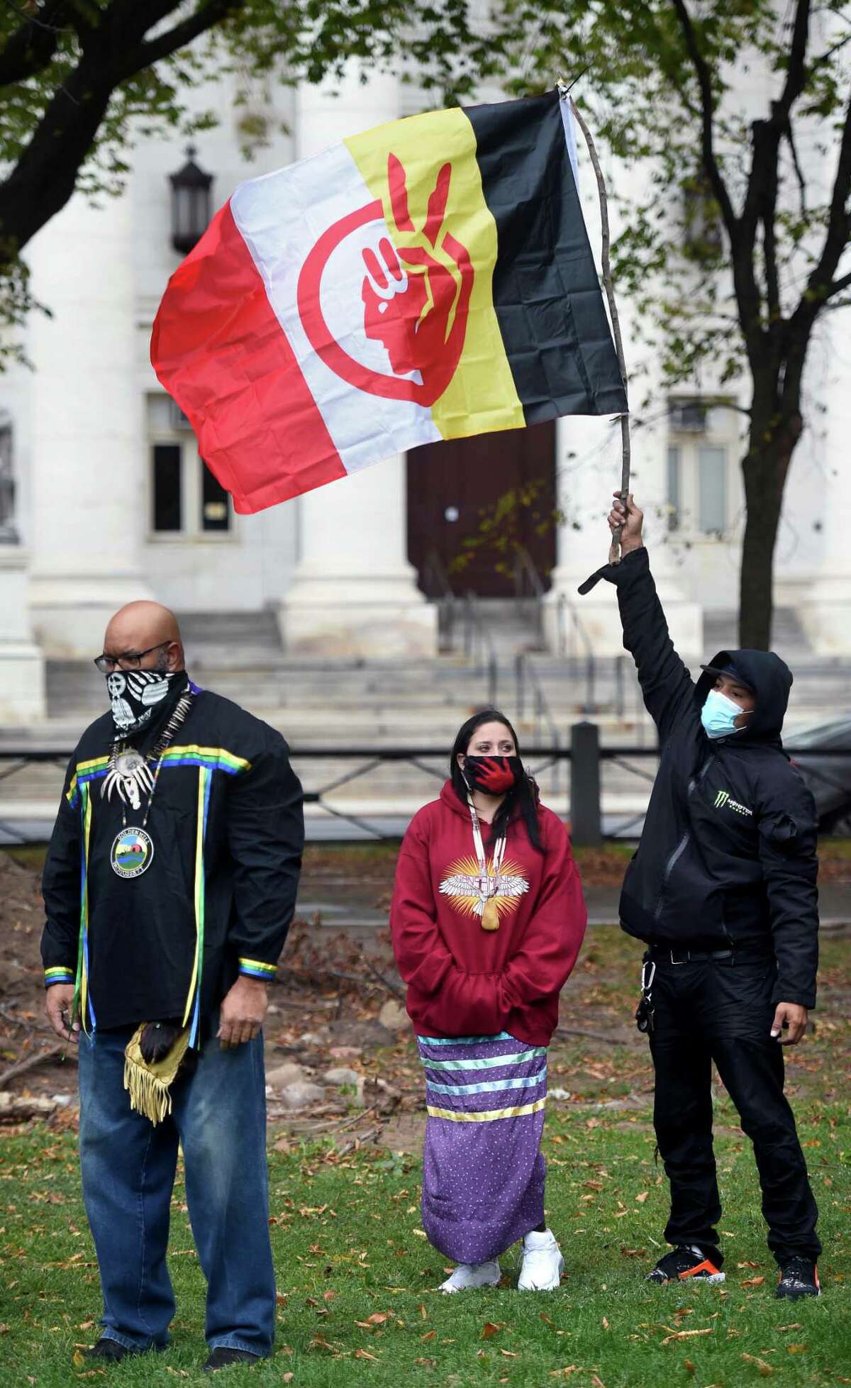 From left, Richard Cowes or Soaring Bear, Rachel Massaro and Radames Figueroa participate in a celebration of Indigenous Peoples' Day on the New Haven Green on October 12, 2020. Figueroa holds a flag of the American Indian Movement. For Clement, Monday’s holiday brought out an array of emotions about the Indigenous experience. Last year, a statue of Christopher Columbus stood tall in Wooster Square Park. Since then, community activism led to the removal of the statue of the explorer who is a symbol of genocide for Indigenous people. Although the city has not recognized Indigenous Peoples Day, it also no longer recognizes Columbus Day, renaming it “Italian Heritage Day.” The school district recognizes the day as Indigenous Peoples Day following a Board of Education vote this year.
