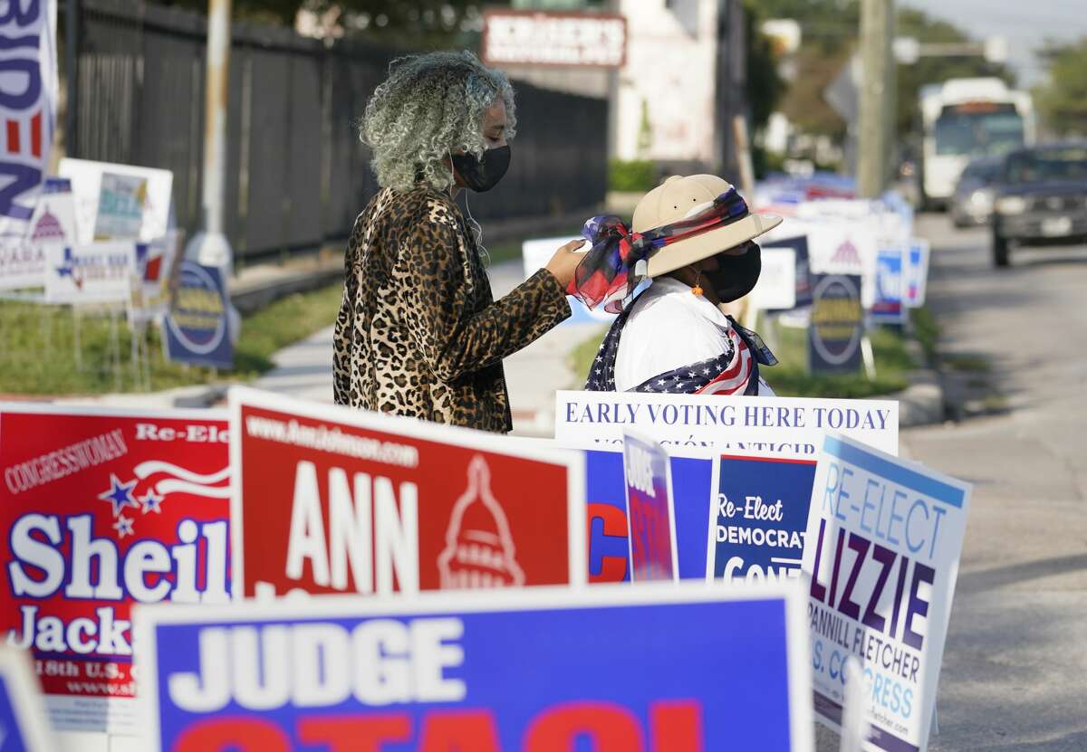 People walk by signs outside the Metropolitan Multi-Services Center, 1475 W. Gray St., during the first day of early voting Tuesday, Oct. 13, 2020 in Houston.