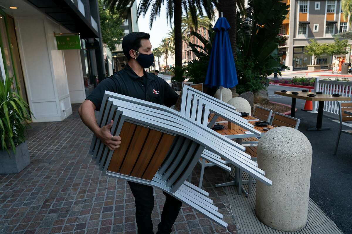Marcus Hoang sets up outdoor seating for dinner at Ozuma along Santana Row in San Jose in July. Some health experts continue to warn against indoor dining, making outdoor