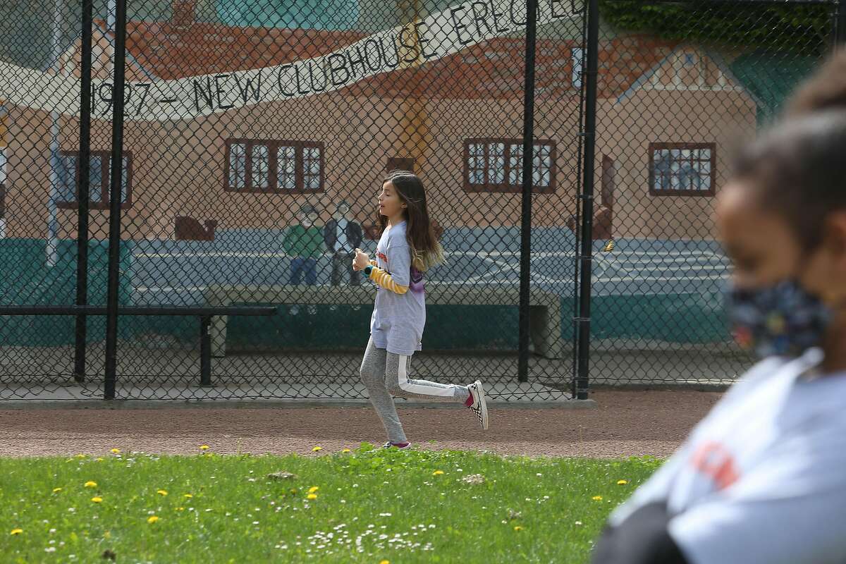 One student attending the emergency child care center at Excelsior Playground runs laps on a field while another waits their turn on Monday, May 11, 2020 in San Francisco, Calif.