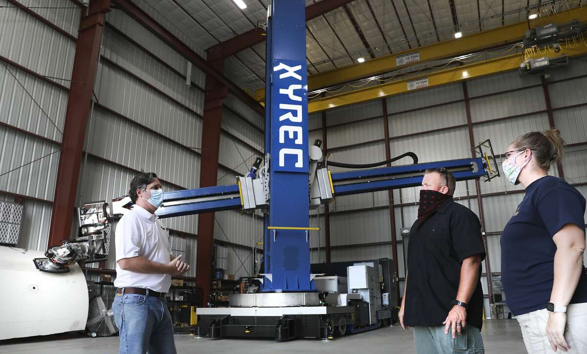 Paul Evans, left, Director of Research and Development at Southwest Researc Institute, discusses the operations of the LCRR with Lucky Nichols, center and Terri Nichols, both of XYREC. The Laser Coating Removal Robot engineered by XYREC, is a 72-foot-tall paint stripping machine that will be used to remove paint from aircraft, on Tuesday, Oct. 13, 2020.