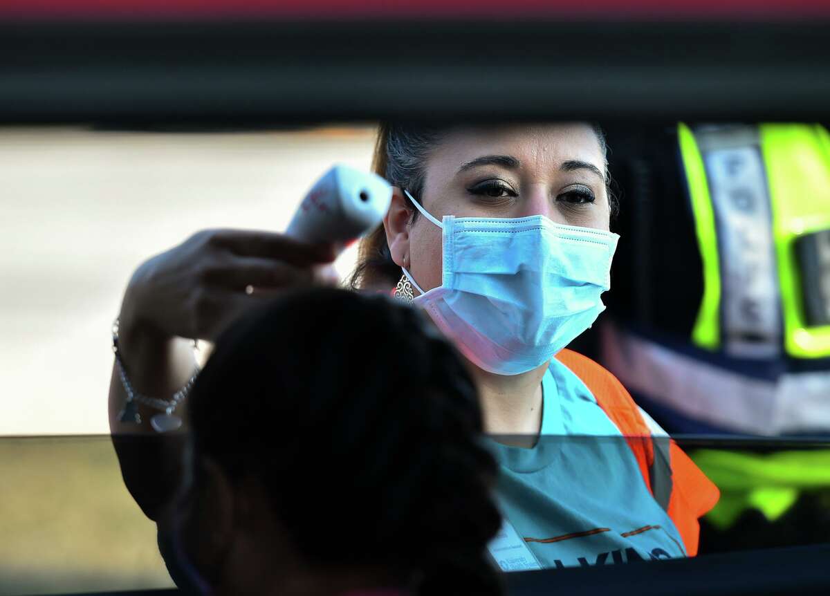 Pamela Reyes checks temperatures as people arrive during a drive-thru flu shot event at Nelson Wolff Stadium on Saturday.