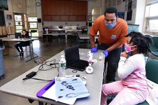 Staff member Jeremy Cooper, right,  assists second-grader Genelle Green,  7, at the New Haven Public School’s learning hub on Ella Grasso Boulevard in New Haven on Oct. 15, 2020.