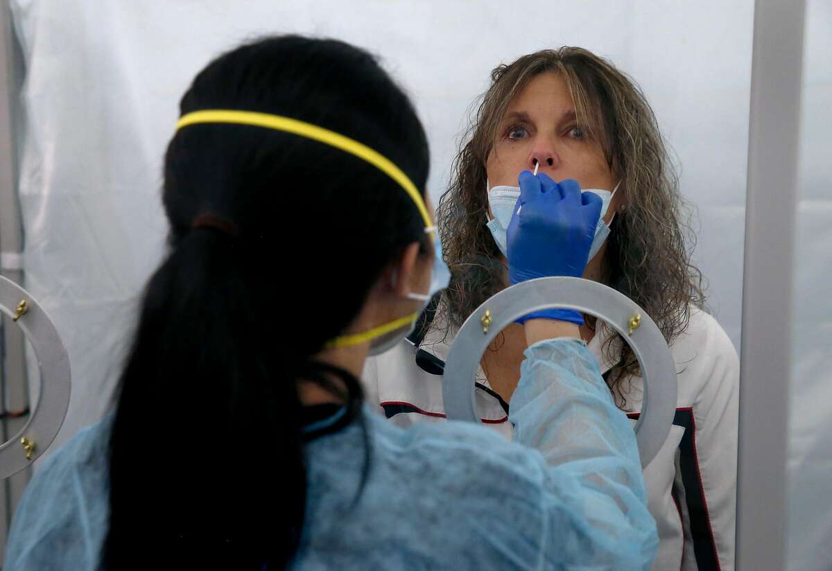 June Lopez, a medical technician with Go Health, collects a sample for a rapid coronavirus test from Theresa Zoller at SFO in San Francisco, Calif. on Thursday, Oct. 15, 2020. Zoller took the test before a flight to Hawaii. As the airline industry sees a modest rise in travel, a rapid COVID-19 testing site has been set up at the airport to provide travelers with documentation of test results to present upon arrival at their final destinations.