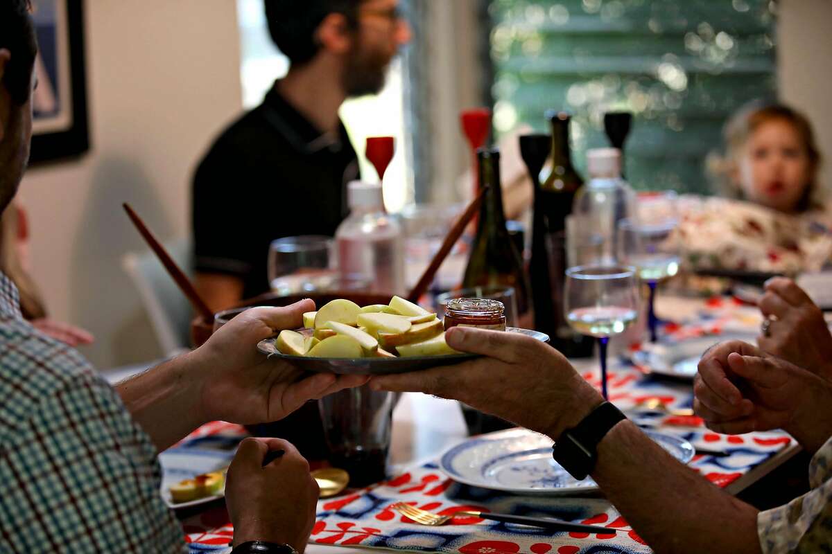 (Left to right) Gabi Moskowitz's brother Jeremy Moskowitz passes a plate of apples and honey to their father Larry Moskowitz during dinner for Rosh Hashanah on Friday, September 18, 2020, in Novato, Calif. Gabi is celebrating with her family with a small dinner at home.