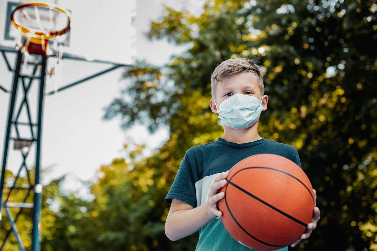 A child holds a basketball while wearing a face mask.