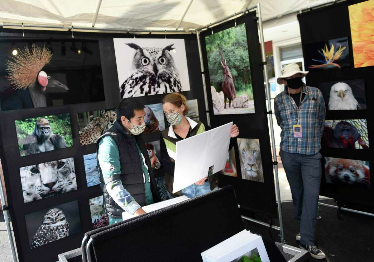 Stamford's Philip Schweiger and Katie Haas browse photos from Bruce Franklin's Fine Art Kingdom booth at the Stamford Downtown Arts & Crafts on Bedford Street event in Stamford, Conn. Sunday, Oct. 18, 2020. The arts and crafts show and sale returned for a second time as Bedford Street closed down to traffic to allow folks to browse more than 20 stands and enjoy outdoor dining with extended outdoor patio cafes. Local and regional vendors displayed a variety of work including paintings, photography, sculpture, candles, garments, jewelry, hats and gloves, and much more.