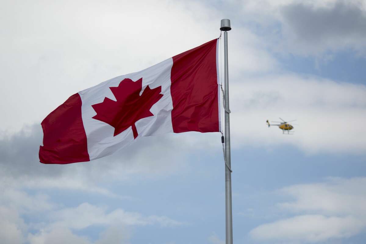 A helicopter flys past a Canadian flag in Niagara Falls, Ontario, Canada, on Wednesday, June 21, 2017. Photographer: Brent Lewin/Bloomberg ORG XMIT: 700073261