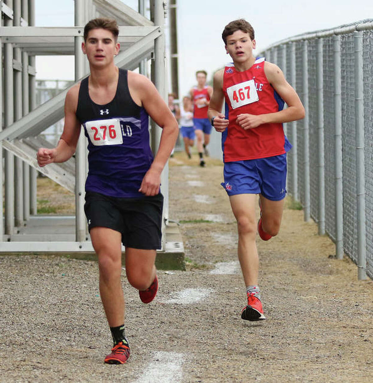 Litchfield’s Camden Quarton (left) and Carlinville’s Will Meyer run the narrow path behind the bleachers at Southwestern’s football field Monday during the SCC Meet in Piasa. Quarton and Meyer held those positions in the final mile to finish second and third, respectively.