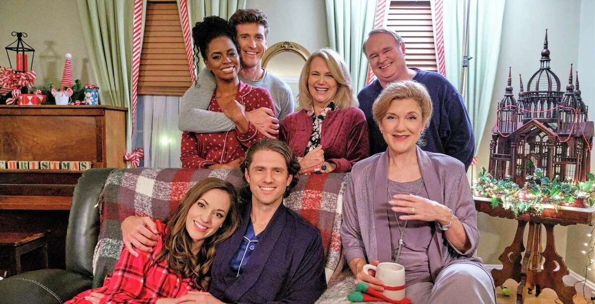 In “One Royal Holiday,” premiering Oct. 31 on Hallmark, Anna (Laura Osnes), far left on couch, offers a stranded mother and son (Aaron Tveit), middle on couch, shelter during a blizzard, and discovers they’re royalty. Also pictured: Victoria Clark, Krystal Joy Brown, Bradley Rose, Geraldine Leer and Tom McGowan.
