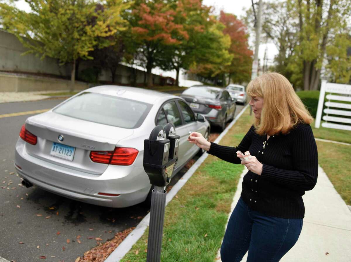 Marianne Hilmer feeds the meter for her car parked on Benedict Place in Greenwich, Conn. Wednesday, Oct. 21, 2020. Hilmer's street does not offer residential parking permits. She is forced to try to find street parking near her building and feed the parking meter in two hour increments throughout the day.