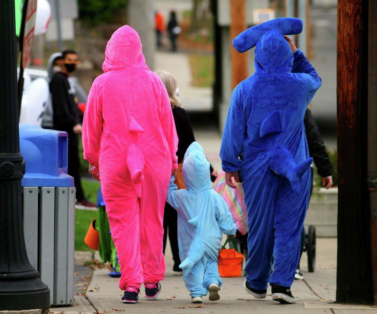 Dressed up as a family of sharks, Ashley and Ralph Dellaventura, of Stratford, walk with their child Avery, 2, as they wander through downtown Milford, Conn., taking part in a safe, socially distant way to enjoy the Halloween holiday on Saturday Oct. 24, 2020. Sponsored by Spinnaker Milford, participating shops put a scarecrow out front and offered treats to local kids.