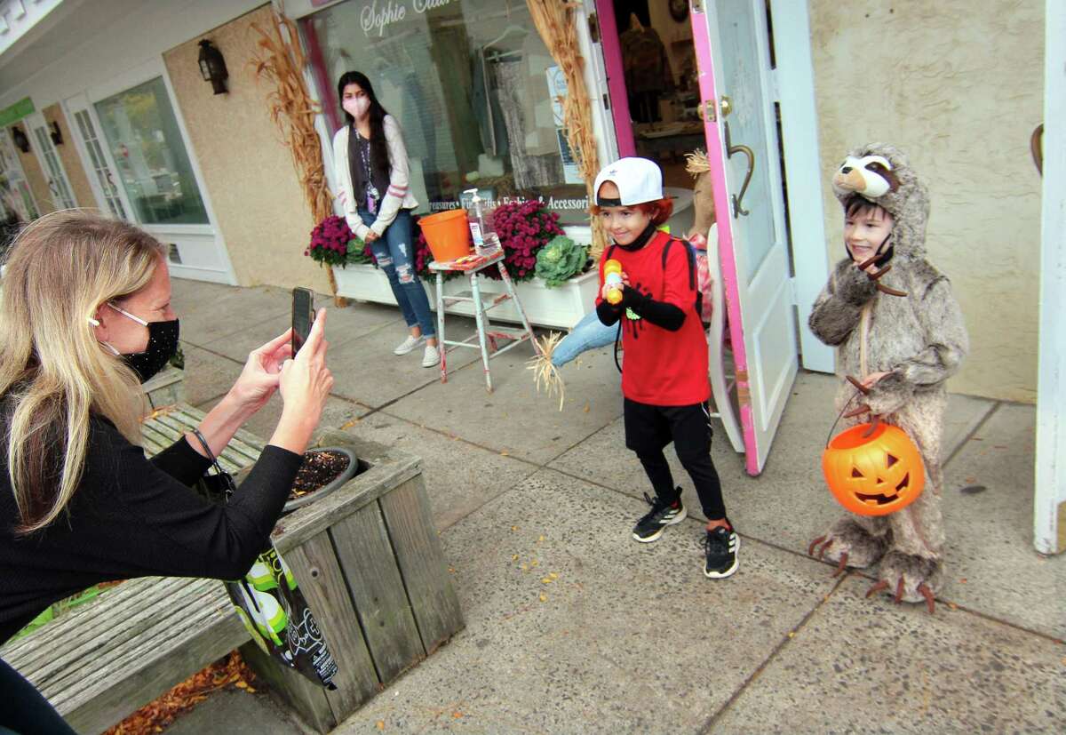 Jenn Field, of Orange, takes photos of her son Phoenix Field, 5, and his friend Miles Yuen, 5, at right, as they take part in a safe, socially distant way to enjoy the Halloween holiday in downtown Milford, Conn., on Saturday Oct. 24, 2020. Sponsored by Spinnaker Milford, participating shops put a scarecrow out front and offered treats to local kids.