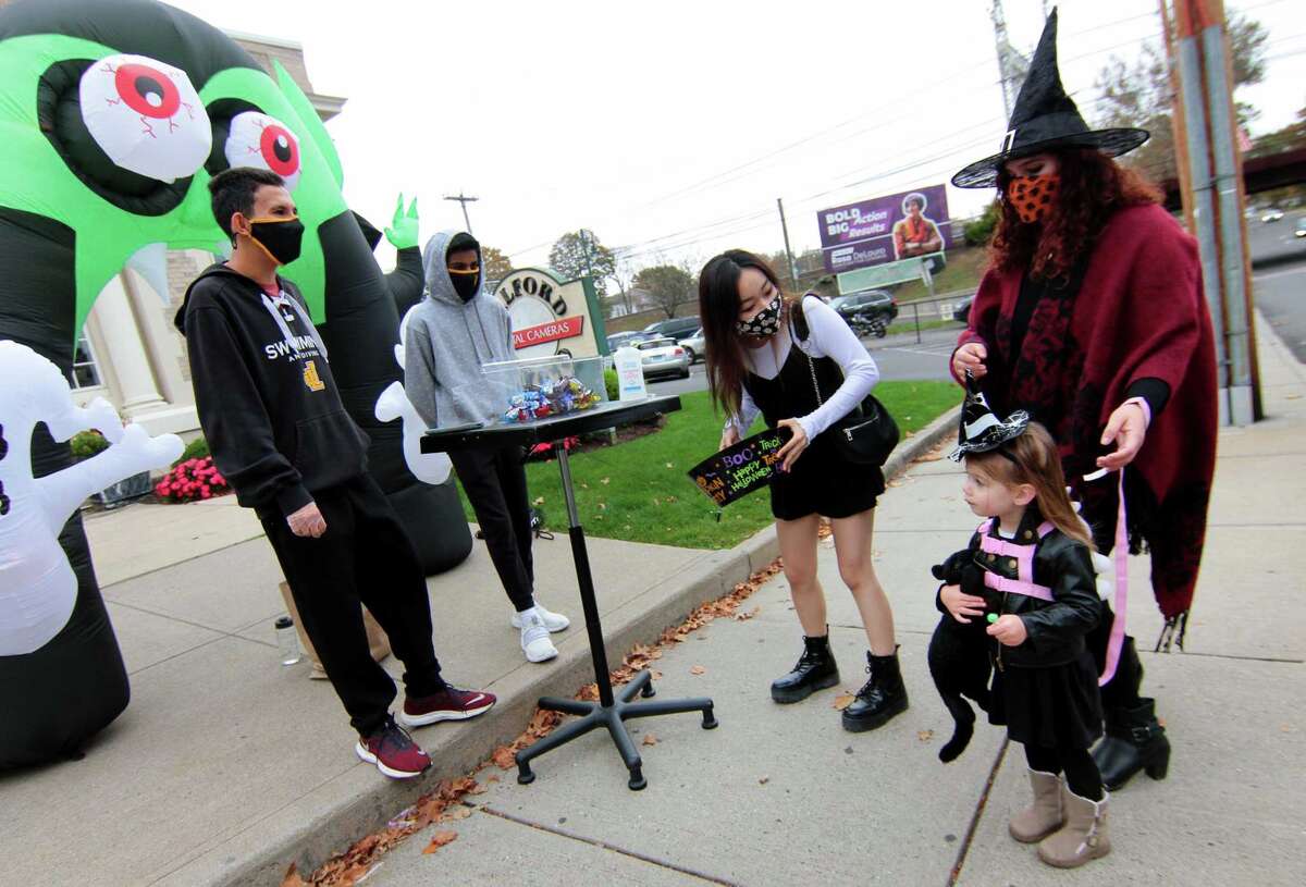 Natalie Purcell, 10, of Milford, gets candy in front of Milford Photo with her mom Agata, as they take part in a safe, socially distant way to enjoy the Halloween holiday in downtown Milford, Conn., on Saturday Oct. 24, 2020. Sponsored by Spinnaker Milford, participating shops put a scarecrow out front and offered treats to local kids.