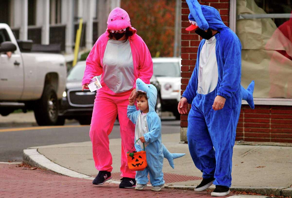 Dressed up as a family of sharks, Ashley and Ralph Dellaventura, of Stratford, walk with their child Avery, 2, as they wander through downtown Milford, Conn., taking part in a safe, socially distant way to enjoy the Halloween holiday on Saturday Oct. 24, 2020. Sponsored by Spinnaker Milford, participating shops put a scarecrow out front and offered treats to local kids.