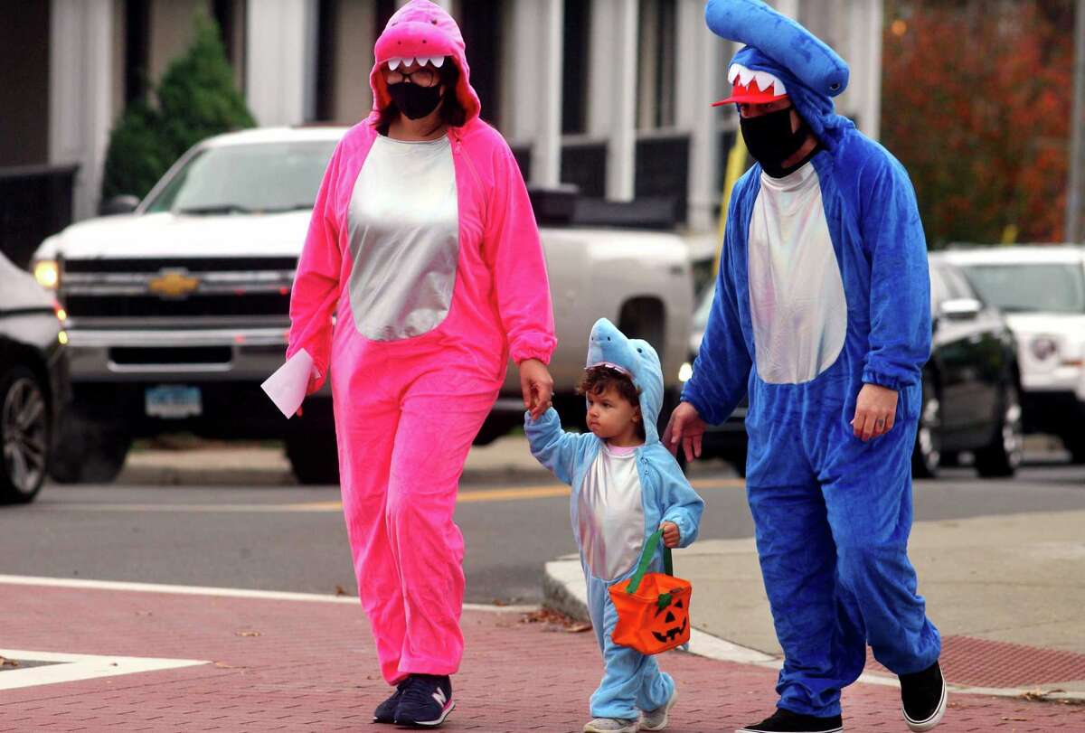 Dressed up as a family of sharks, Ashley and Ralph Dellaventura, of Stratford, walk with their child Avery, 2, as they wander through downtown Milford, Conn., taking part in a safe, socially distant way to enjoy the Halloween holiday on Saturday Oct. 24, 2020. Sponsored by Spinnaker Milford, participating shops put a scarecrow out front and offered treats to local kids.