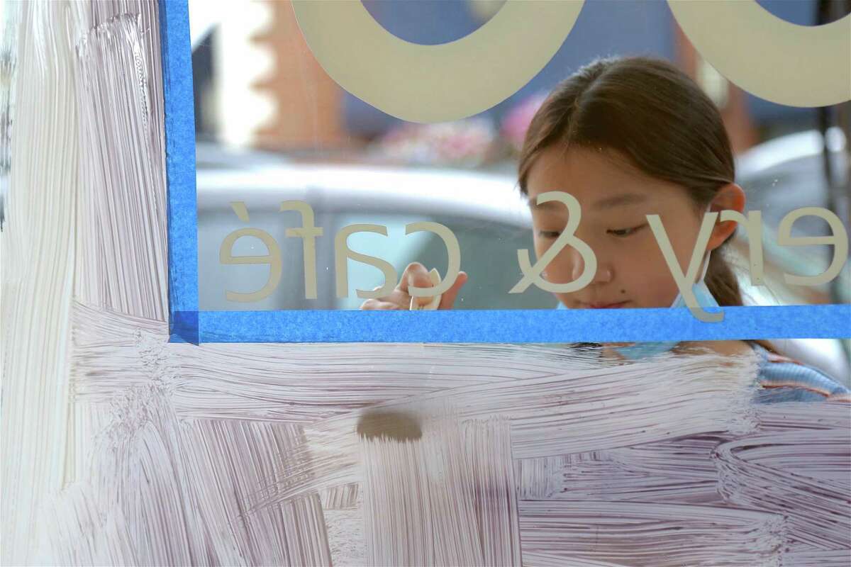 Jingjing He, 11, of Darien, paints the window of UCBC on the Post Road on Saturday morning.