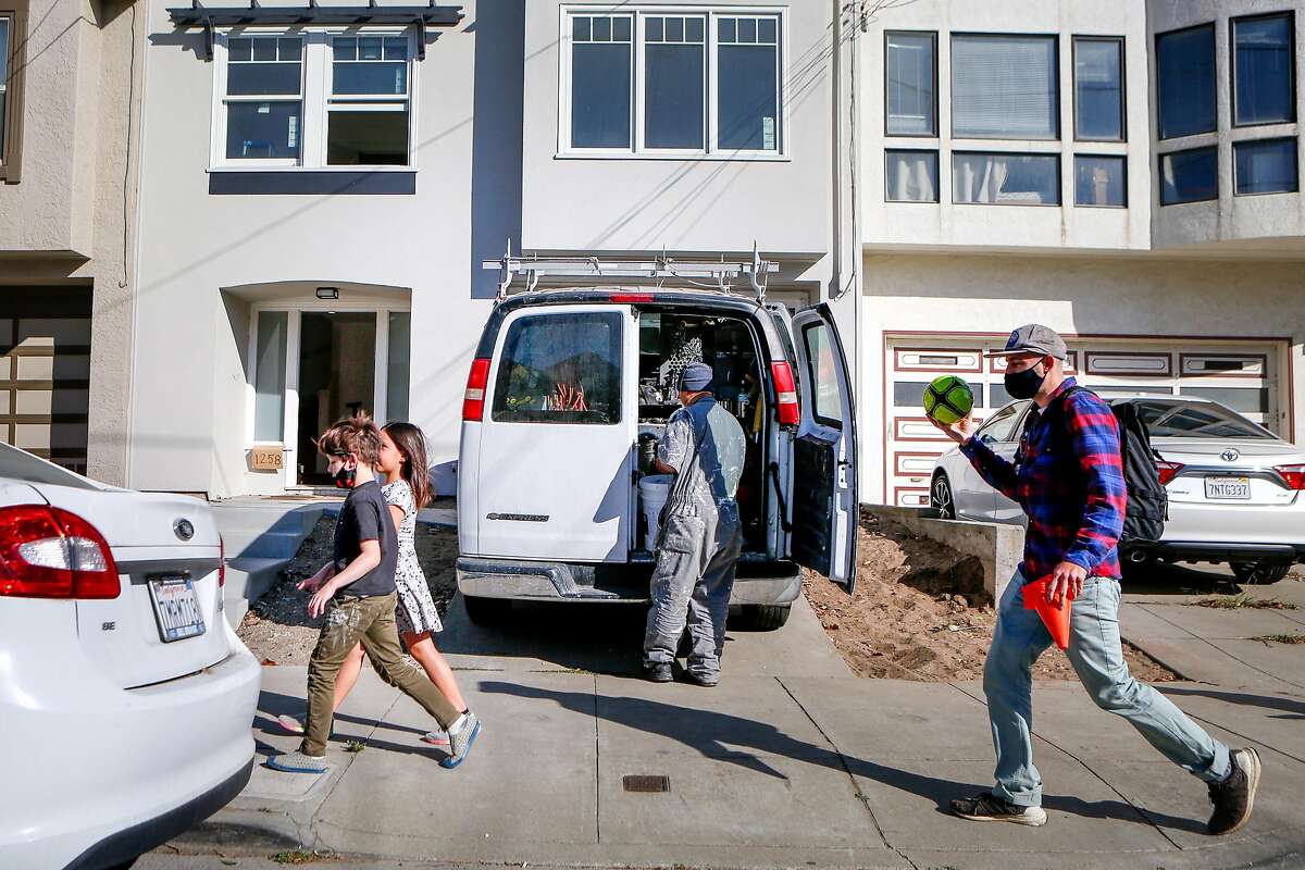 Cameron Adler (right), Leo, 7, and Abigail, 7, walk past Sonny Yang as he pulls materials from a work van outside of a single family home that's being renovated for sale in the Outer Sunset on Monday, October 26, 2020 in San Francisco, Calif.