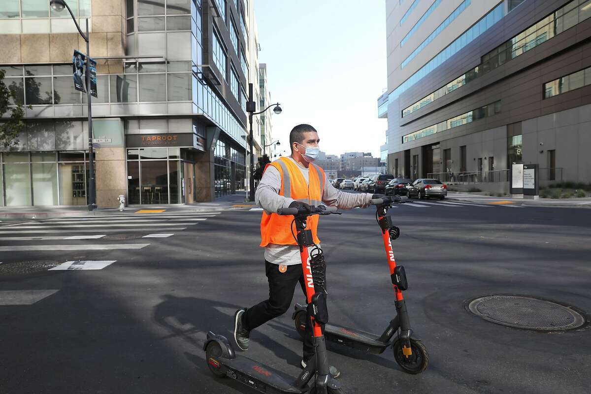 Michael Delgado, SPIN operations specialist, walks scooters down 16th street to a rack while deploying scooters at Chase Center on Monday, October 19, 2020 in San Francisco, Calif.