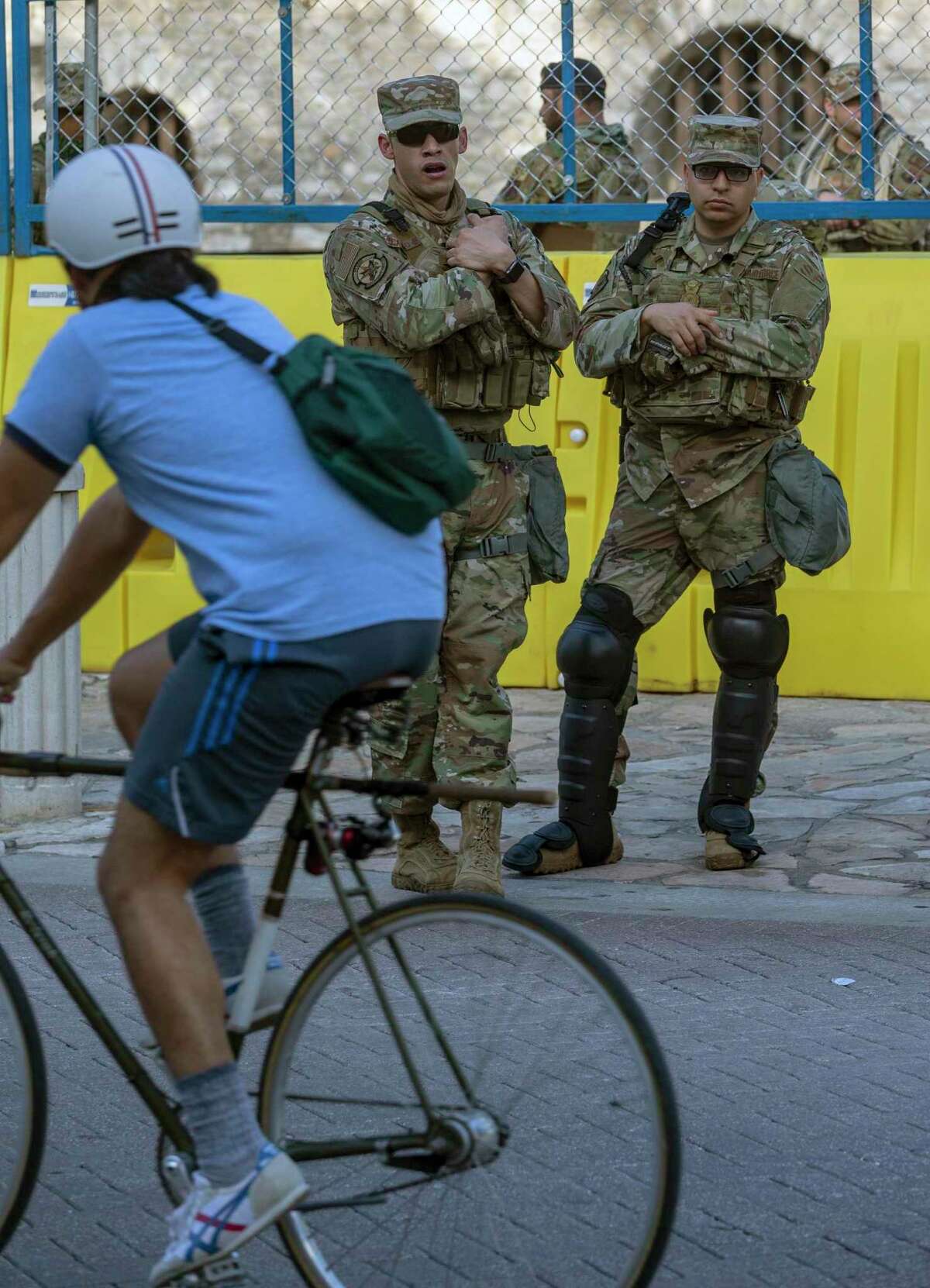 Texas Air National Guard airmen watch a bicyclist ride past the Alamo on June 3 . The guardsmen were part of a heavy military and police presence there to keep ongoing protests over racial justice issues out of Alamo Plaza.