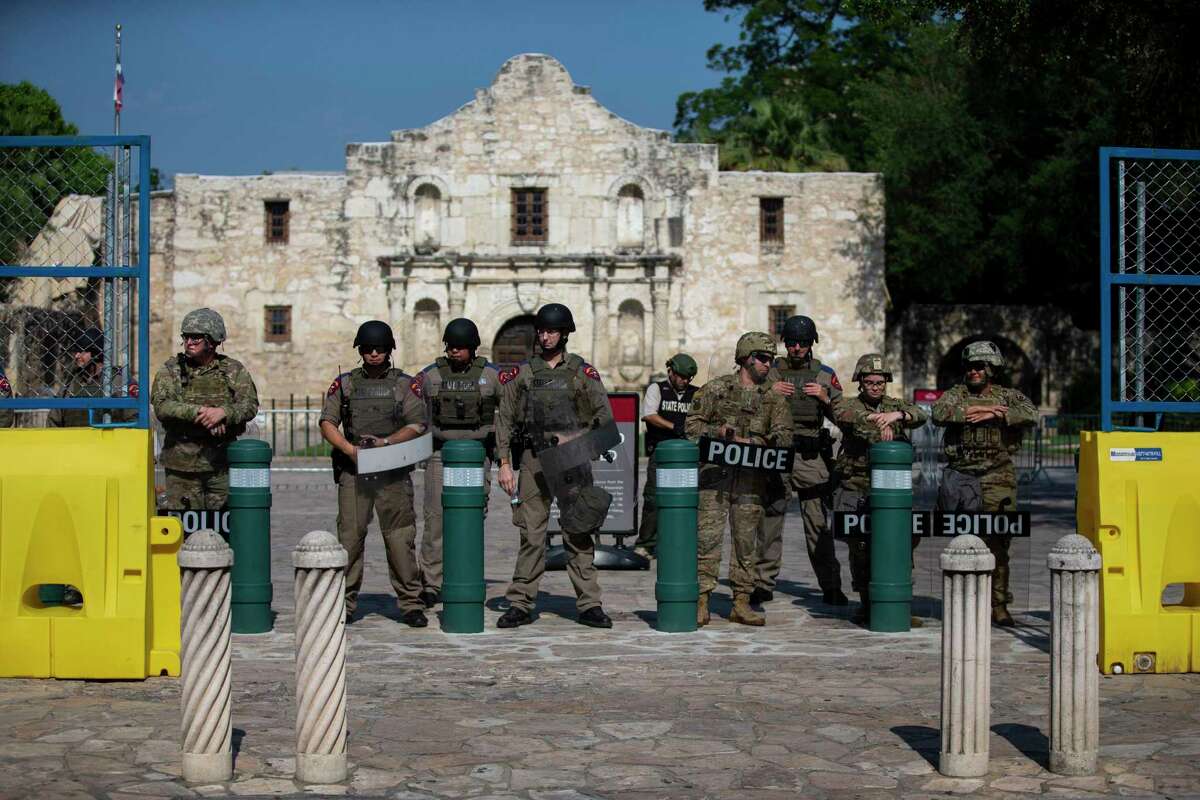 Texas state police and national guard personnel stand at the entrance to Alamo Plaza as protesters march nearby on June 9.