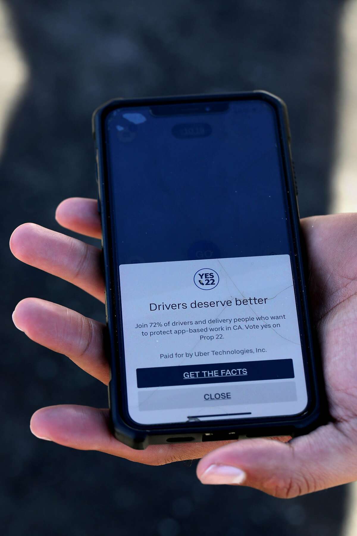 Uber driver Jorge Torres, 29, holds his phone displaying a Prop. 22 ad that the company placed in its driver app. Some drivers have complained that the campaign ads are coercive.