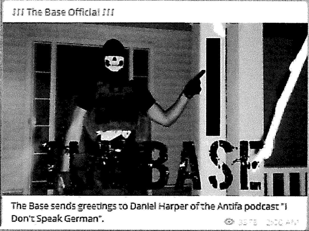 A screen shot of an arrest affidavit shows a photograph that was uploaded to "The Base" channel on the publicly available social media platform Telegram. According to the affidavit, the photograph shows Justen Watkins, 25, of Bad Axe, wearing a black skull mask, a Totenkopf shirt, camouflage pants, and a tactical plate carrier with rifle magazines that has a patch of the logo for "The Base" visible on the front of the vest.