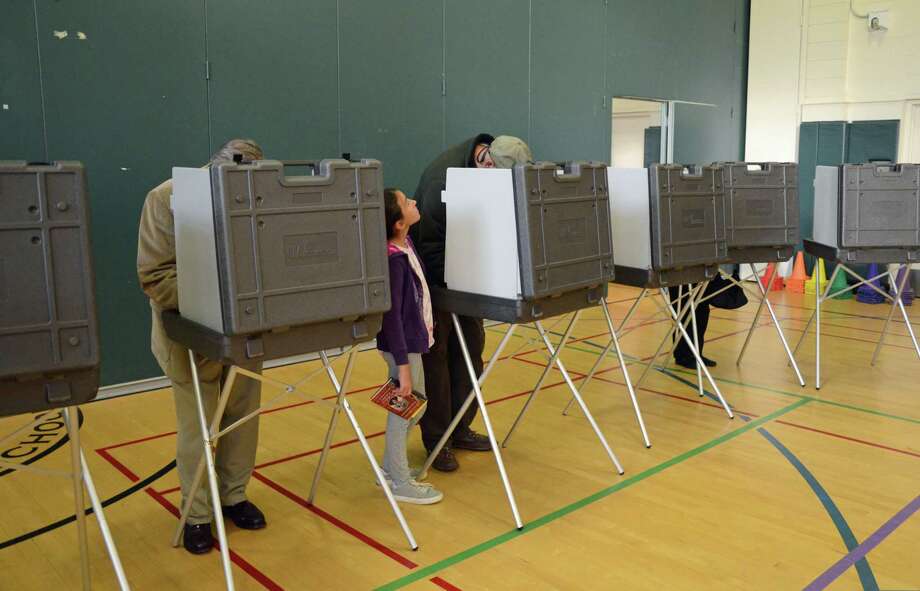 A young girl stands next to a voter during a recent day of voting in Greenwich. Photo: Tatiana Flowers / Hearst Connecticut Media / Greenwich Time