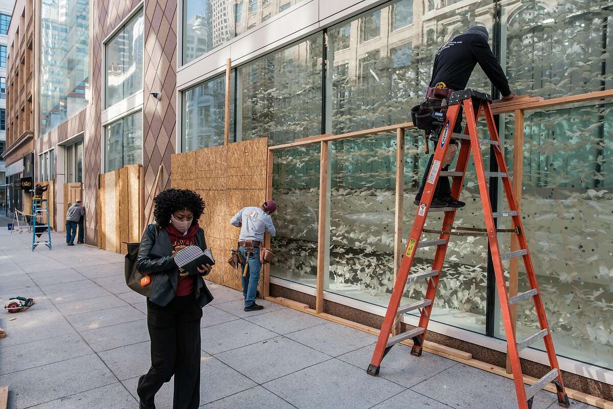 A pedestrian walks past a construction crew as they board up shop windows near Union Square in San Francisco.