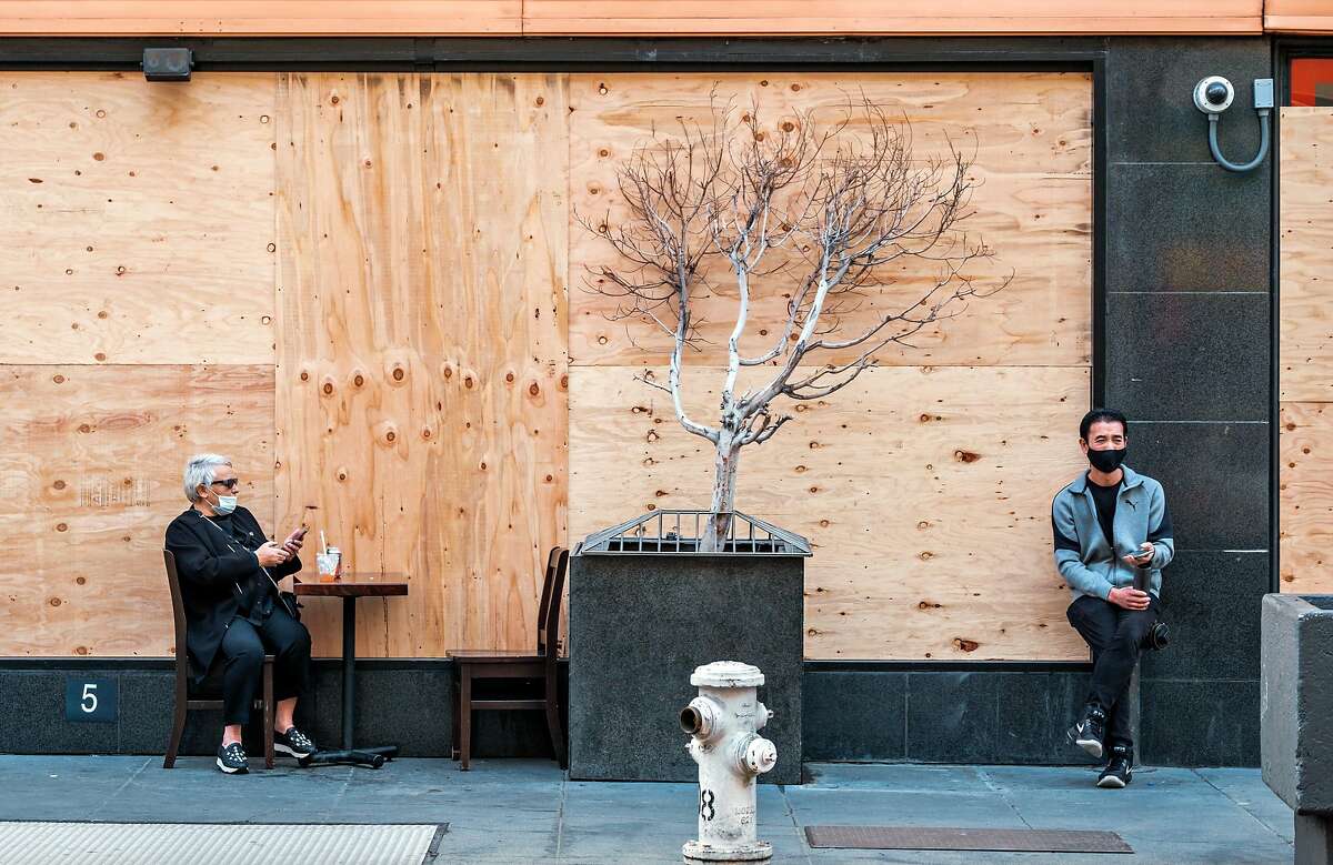 People sit near recently boarded up windows at Macy’s near Union Square in San Francisco on Friday. Cities and business are preparing for election night unrest.