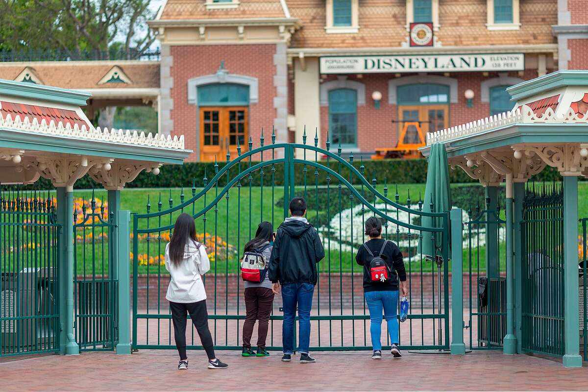 In this file photo taken on March 14, 2020 people stand outside the gates of Disneyland Park on the first day of the closure of Disneyland and Disney California Adventure theme parks, in Anaheim, Calif.