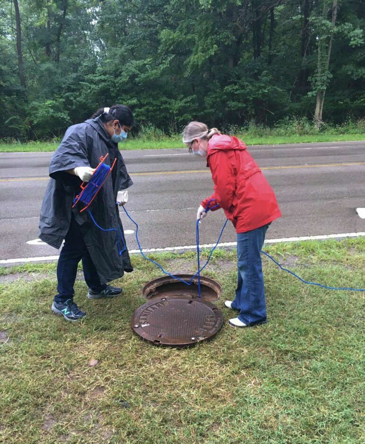 Researchers Becca Ives and Nishita D'Souza lower a container into a manhole to sample wastewater at Michigan State University. (Capital News Service photo)