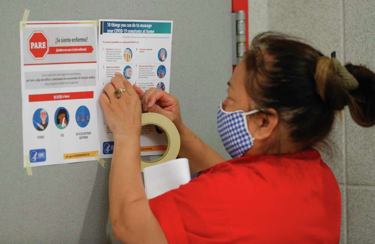 Splendora custodian Rosario Flores hangs coronavirus safety and sanitization signs on bathroom doors at Splendora High School Aug. 11 in Splendora. The Splendora ISD board voted unanimously Monday to continue with health and safety protocols, including masks.
