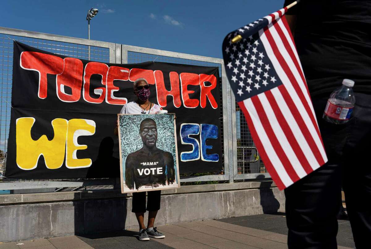 Reva Danforth holds a picture of George Floyd while her pictures is taken in front of a banner that reads "Together We Rise" during a celebratory rally and count the vote event hosted by local activist groups, Saturday, Nov. 7, 2020, at Emancipation Park in Houston.