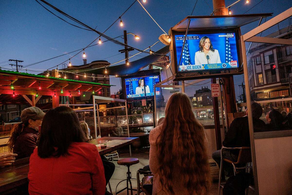 People watch Vice President Elect Kamala Harris speak on television at Piazza Pellegrini in North Beach in San Francisco on Saturday, November 7, 2020.
