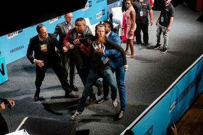During a speech by Sen. Kamala Harris, an animal rights protester is hustled off the stage by security and Harris' husband, Douglas Emhoff (left), at the MoveOn Big Ideas Forum at the Warfield Theater in San Francisco, Calif., on Saturday, June 1, 2019.