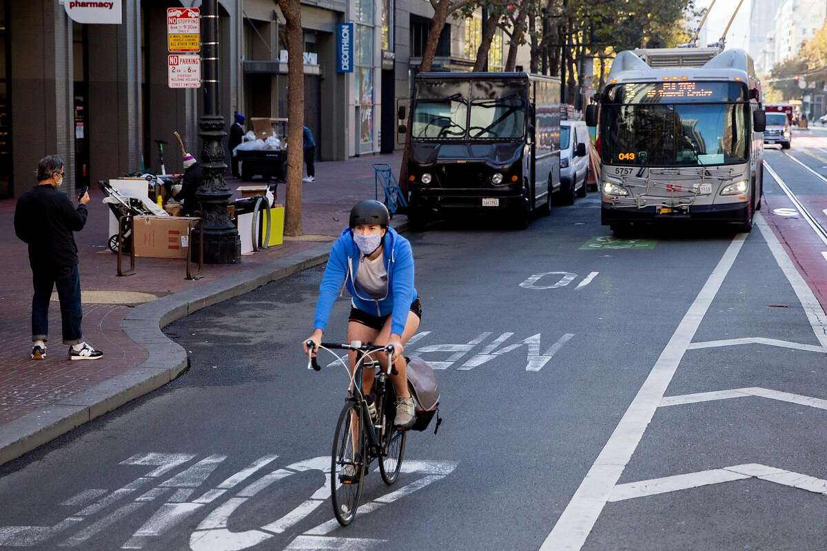 A cyclist bikes in front of a bus near the intersection of 4th and Market street in San Francisco, Calif. Friday, October 30, 2020. The Department of Public Works and the San Francisco Municipal Transportation Authority has been quietly telling stakeholders the past couple weeks that due to budget cutbacks, bicycles will now share a lane along with taxis, paratransit, and commercial vehicles, and Muni busses will use only the center lane instead of curbside stops. The city will save $40 million, but it will still cost $121 million and an additional $7 million for redesign. The plane came to a head at a meeting Tuesday, with city supervisors and bike and pedestrian advocates protesting the sudden change.