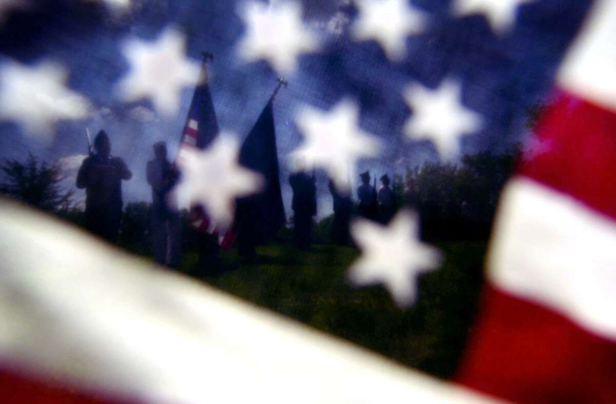 The Hamel American Legion Post 394 color guard is seen through a small United States flag, left near a grave at the German Liberal Cemetery in Medina, Minn., during a Memorial Day ceremony, Monday, May 28, 2001. (AP Photo/The Star Tribune, Richard Sennott)