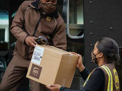 A UPS driver and a driver’s helper unload a package.