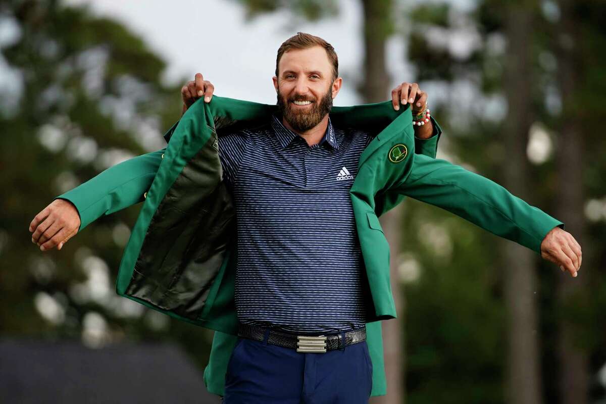 Tiger Woods helps Masters champion Dustin Johnson with his green jacket after his victory at the Masters golf tournament Sunday, Nov. 15, 2020, in Augusta, Ga.