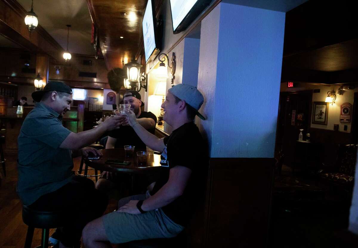 Alex Campos, left, Michael Saathoff, and Kyle Urias toast at The Winchester pub as the establishment opened its doors for the first legal drinks in a San Antonio bar in nearly two months at 12:01 am on Friday, May 22, 2020. County officials say they will close bars that don’t serve food again if the county reaches a positivity rate of 10 percent or higher and stays there for two weeks. The rate was at 9.4 percent Monday.