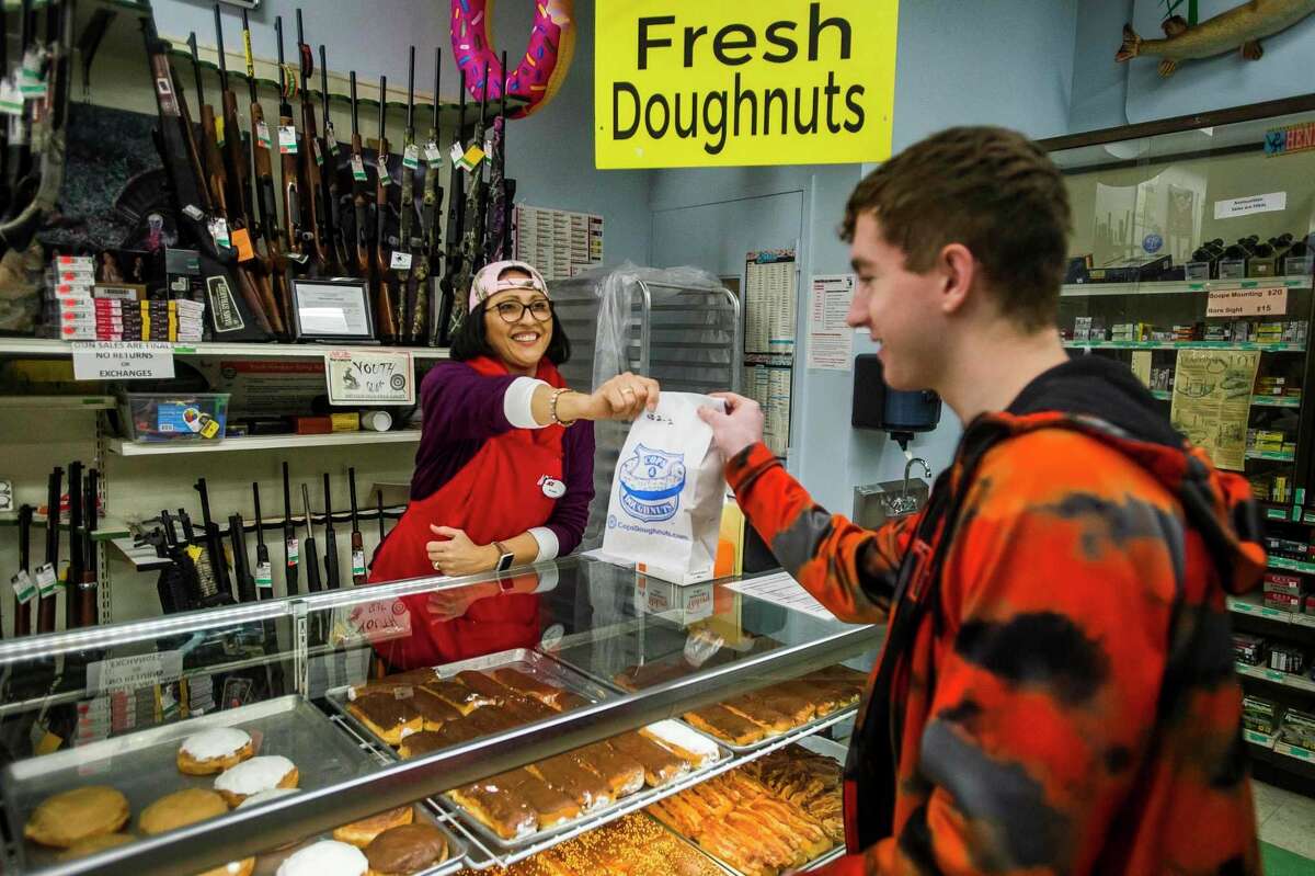 Belinda Kuchek hands a bag of doughnuts to Jake Grames before he makes his purchase Monday morning at Ace Hardware & Sports in Midland. The store now sells doughnuts from Cops & Doughnuts, a popular Clare city bakery. (Katy Kildee/kkildee@mdn.net)