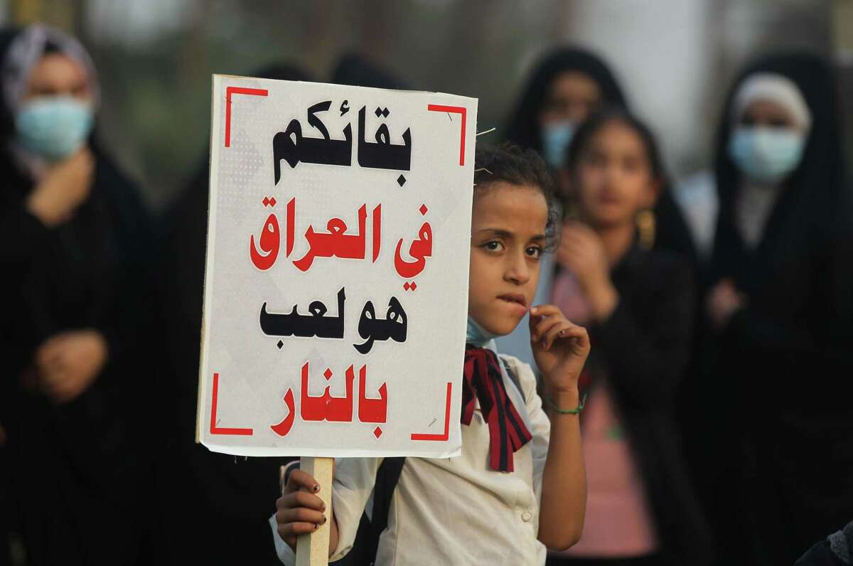 A girl carries a sign reading in Arabic "your remaining in Iraq is playing with fire" during a demonstration outside the entrance to the Iraqi capital Baghdad's highly-fortified Green Zone on November 7, 2020, demanding the departure of remaining US forces from Iraq. - Several hundred protesters gathered in the Iraqi capital on Saturday afternoon to demand US troops leave the country in accordance with a parliament vote earlier this year. (Photo by AHMAD AL-RUBAYE / AFP) (Photo by AHMAD AL-RUBAYE/AFP via Getty Images)